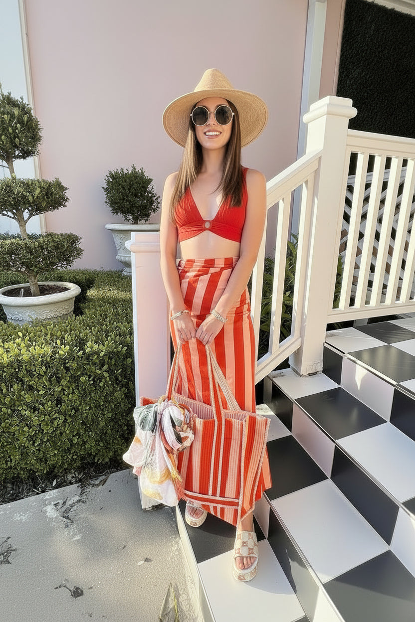 Woman in an orange wrap sarong skirt and straw hat standing on a checkered porch.