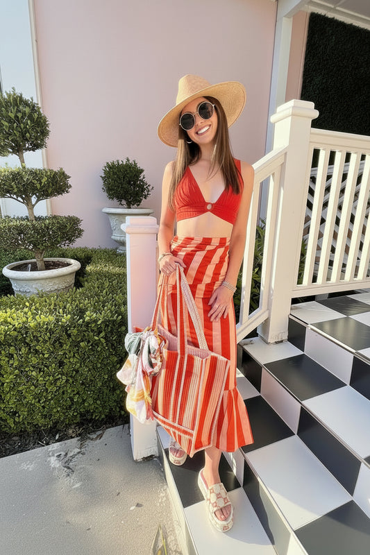 Woman in an orange wrap sarong skirt and straw hat standing on a checkered porch.