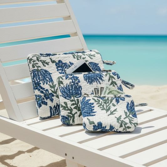 Blue swimsuit and floral waterproof bags on a sandy beach with turquoise water and palm leaves. Perfect for a beach bag.
