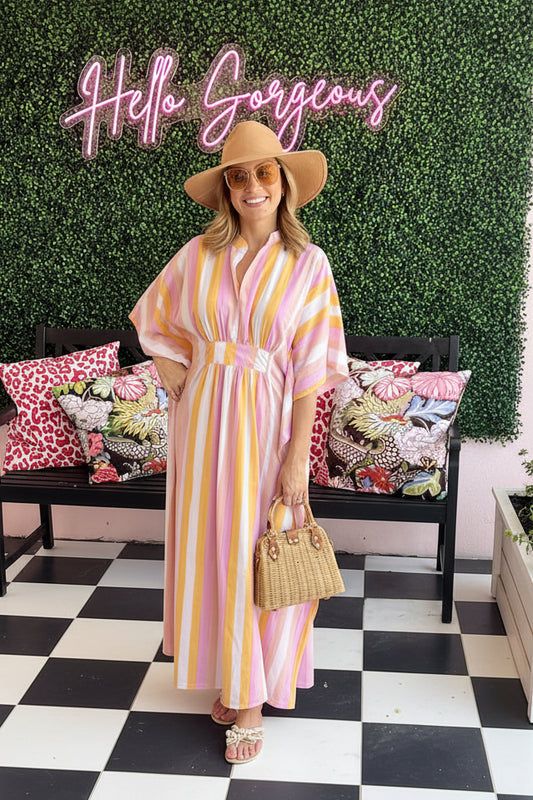 Woman in a pink and yellow striped coverup tunic standing in front of a 'Hello Gorgeous' sign with a bench and pillows in the background.