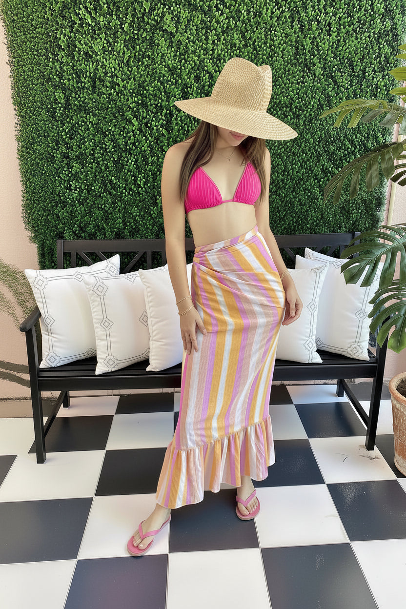 Woman in a pink bikini top and striped skirt standing in front of a 'Hello Gorgeous' sign.
