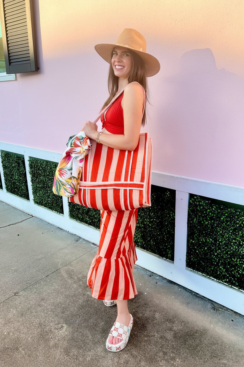 Woman in a red and white striped dress holding a colorful bag against a pink wall.